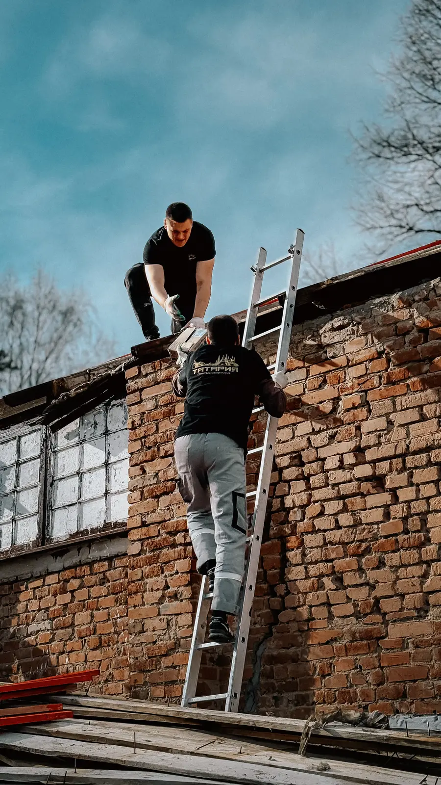 Zwei Handwerker auf einer Baustelle reichen sich auf einer Leiter Material an